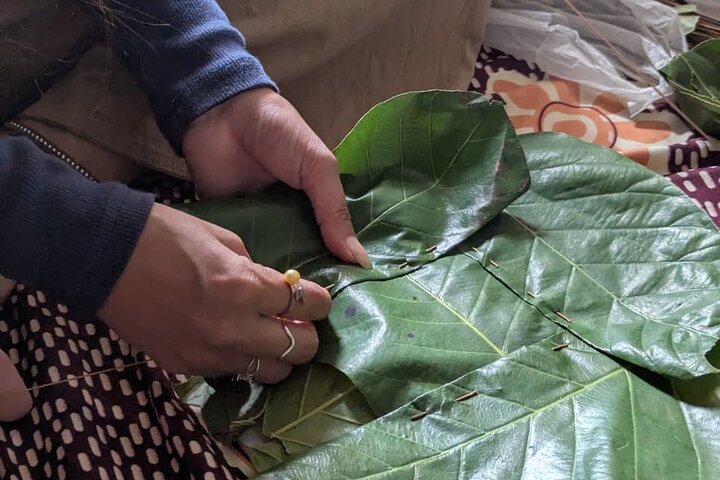 A close-up of hands sewing green sal leaves together with thin bamboo sticks to make an eco-friendly leaf plate