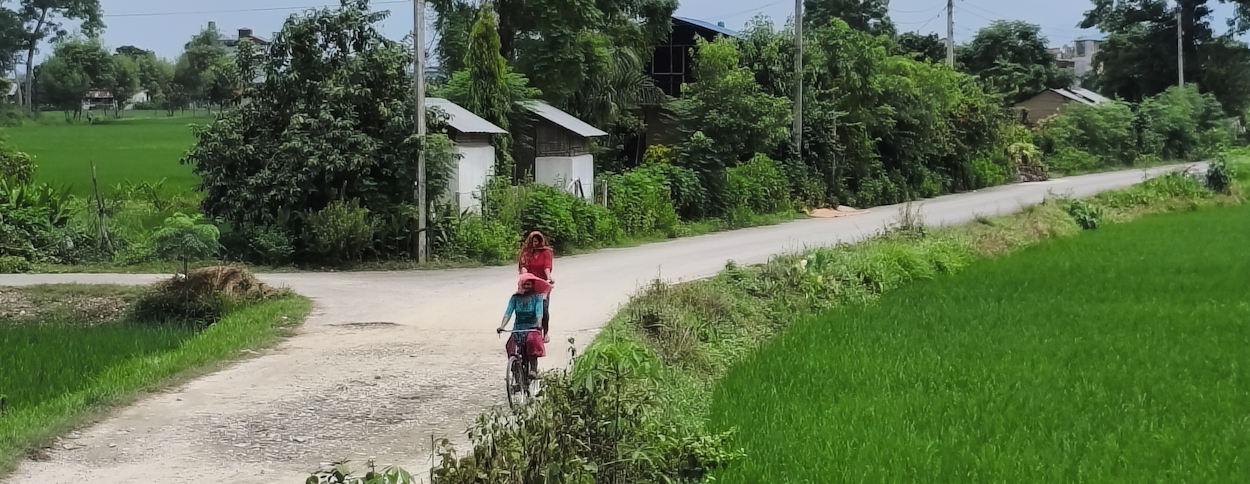 Two local women cycling in rural Sauraha with grasslands and small houses around